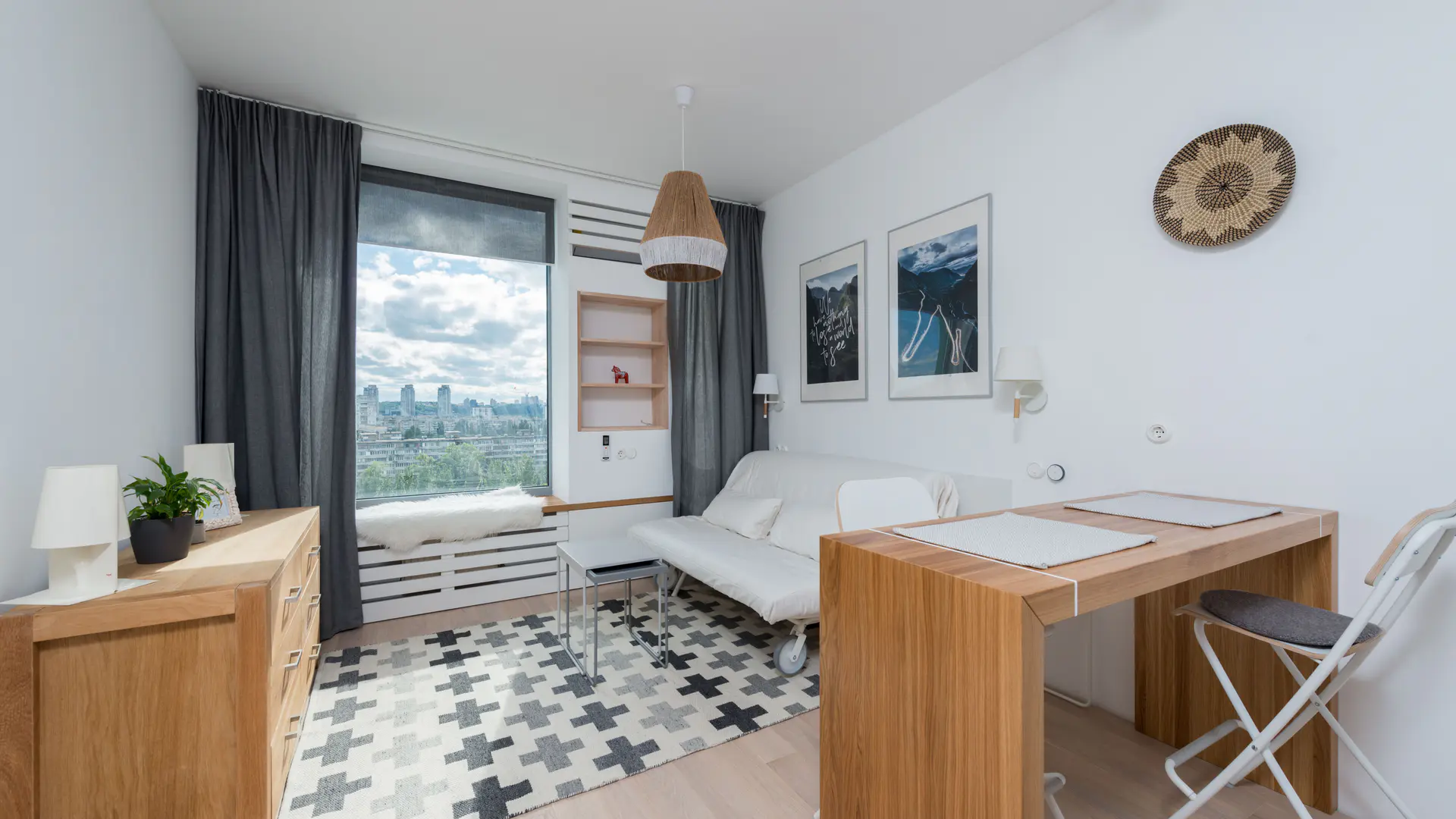Furnished apartment living area in daylight with a desk and a city-facing window